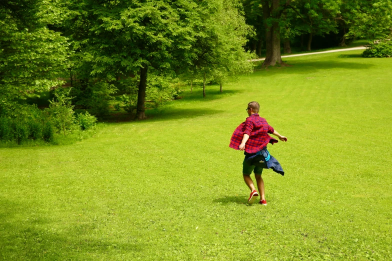 the man is walking through the grass with two frisbees