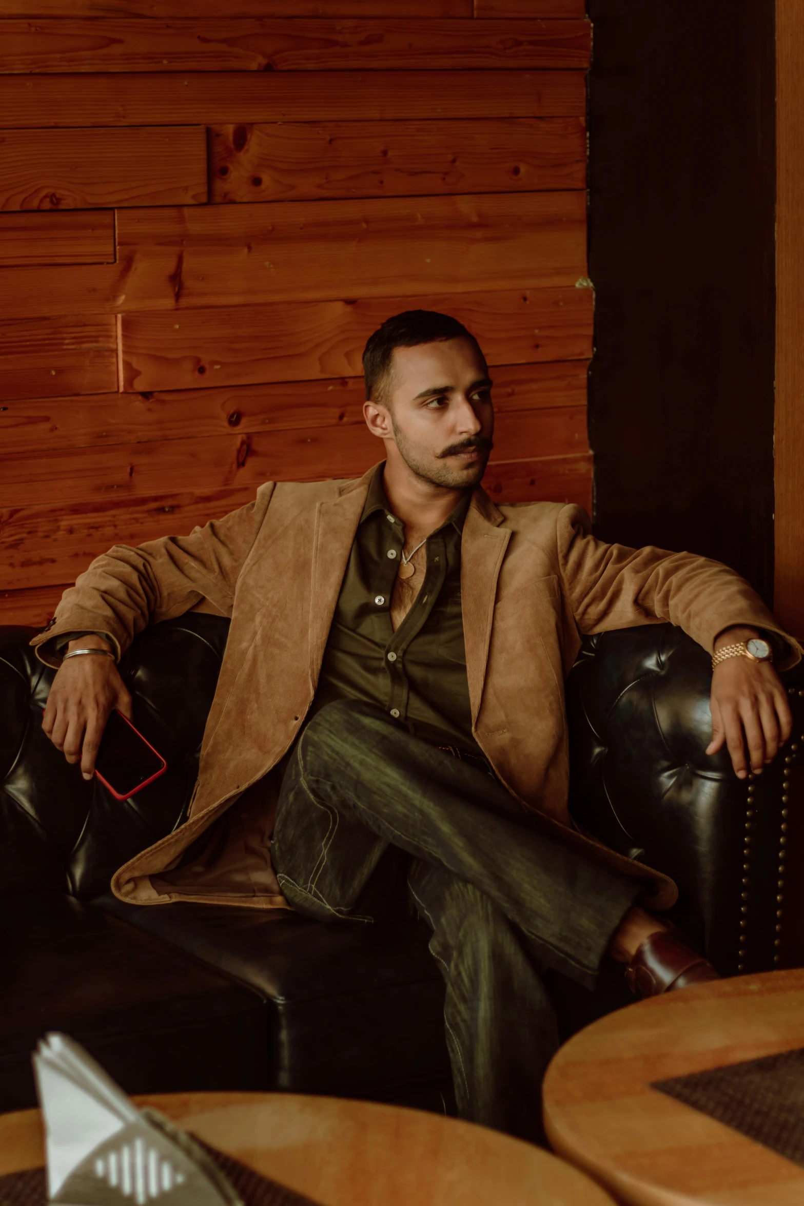 a man sits on a black couch in front of a wood wall