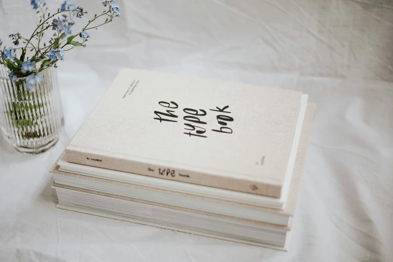 several different types of books stacked next to a glass vase with flowers