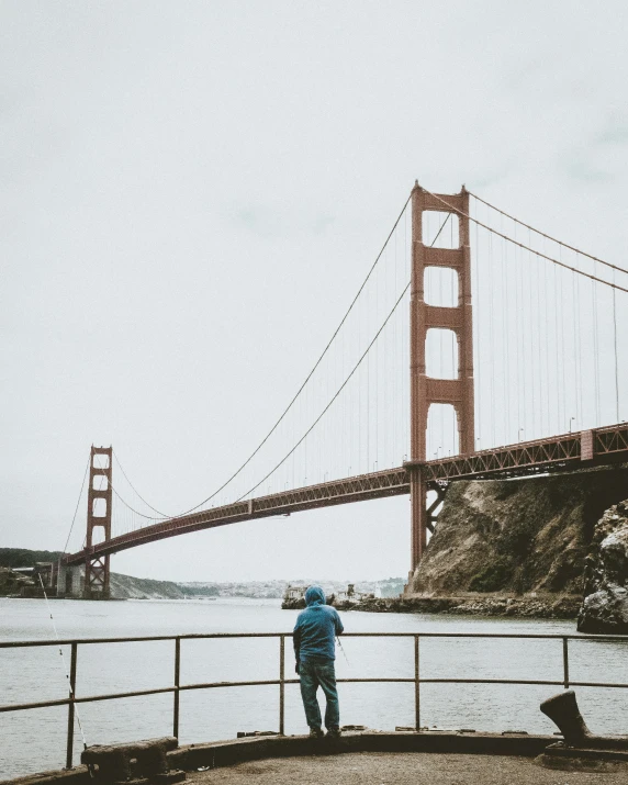 a person standing near the water with a bridge in the background