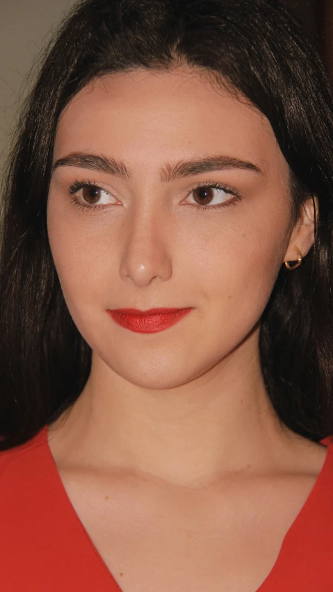 close up view of a woman's face, with a red top and earrings