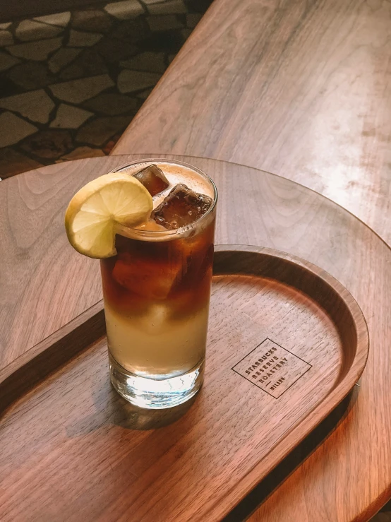 a drink with lemon wedged in on a wooden tray