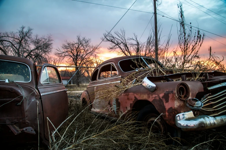 an old truck and another rusted car sit in the grass
