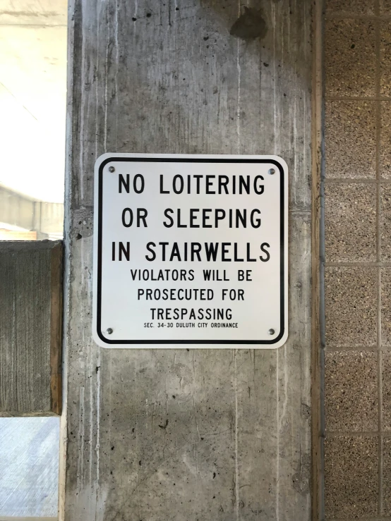 a no littering or sleeping sign attached to a cement column