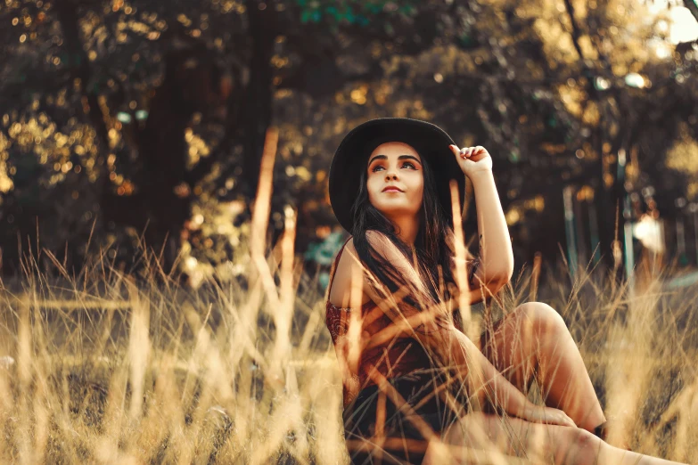 a woman wearing a hat is sitting in tall grass