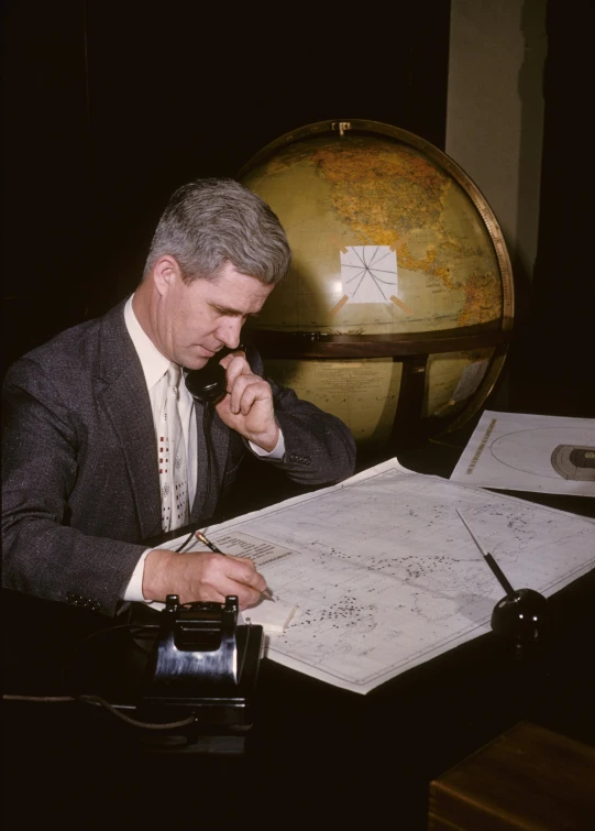 an older man is sitting at a desk and on a telephone