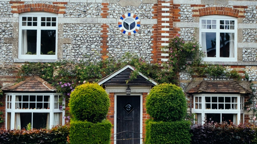 a brick and stucco building with three windows, bushes, and flowers on the side