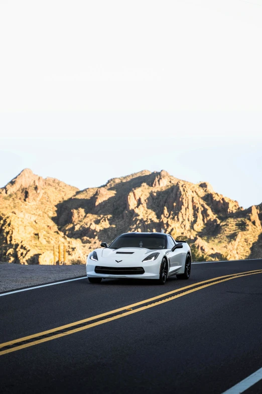 a white car is traveling down the road next to some mountains