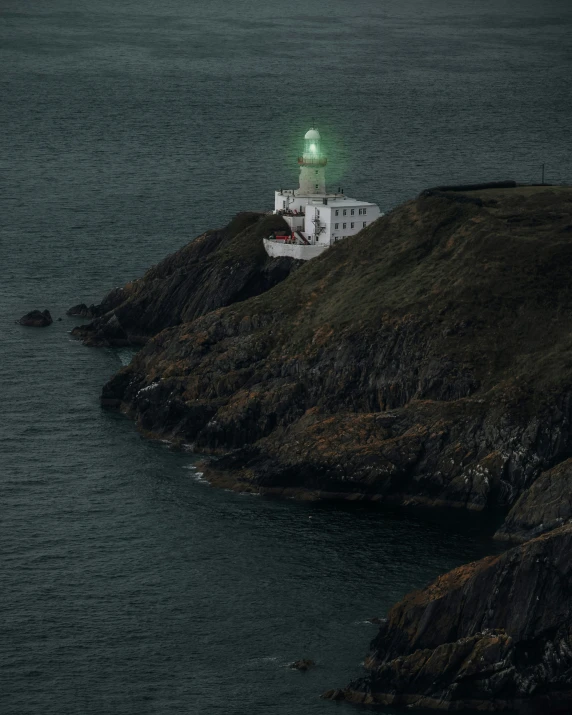 a lighthouse sits on top of a hill by the water