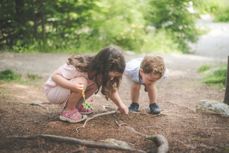 two little girls are bending over to look at a piece of wood