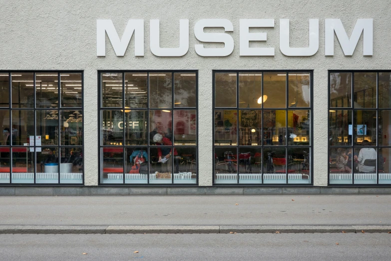 a museum window with three windows and several people sitting in the chairs