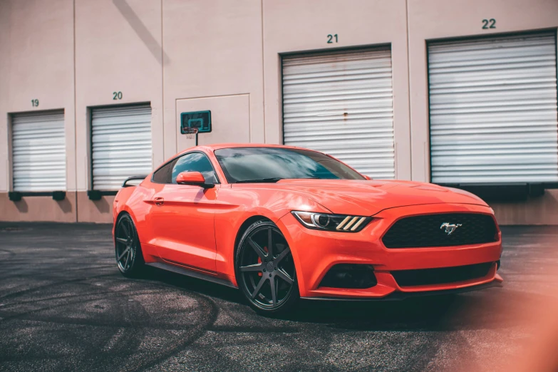 a red mustang parked in front of some garage doors