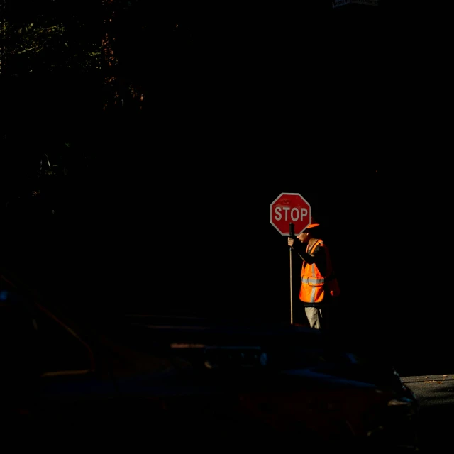 a stop sign and a construction worker are silhouetted against the dark night sky