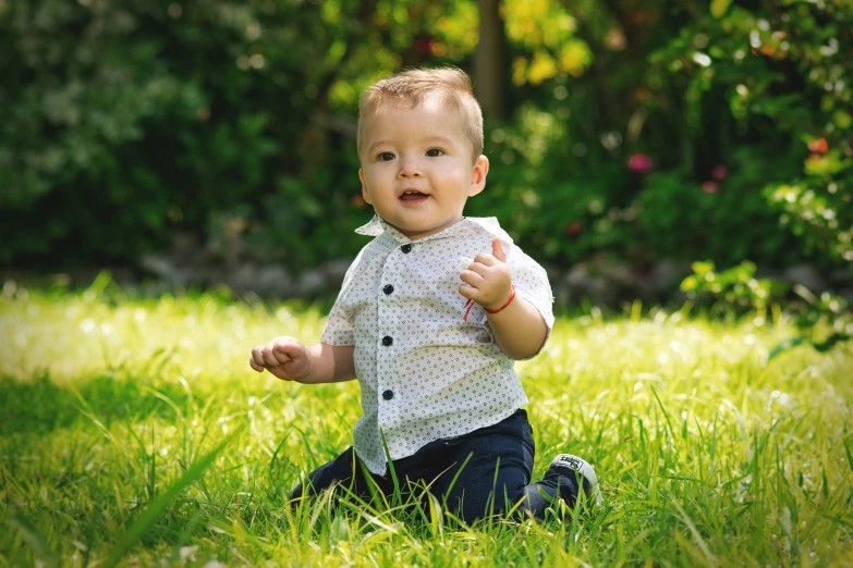 a baby sits in the grass with his hands clasped