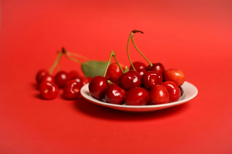 a white plate with cherries and leaves on a red surface