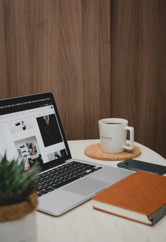 an open laptop sits on a table with two coffee cups