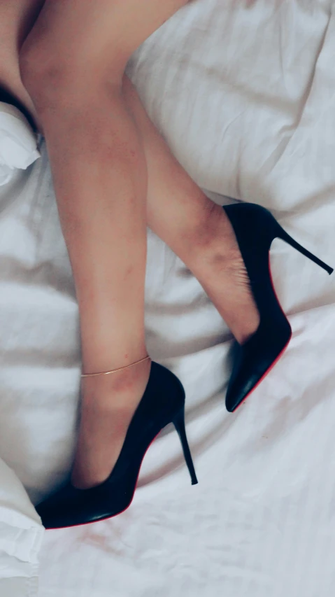 a woman wearing a pair of black heels sitting on a bed