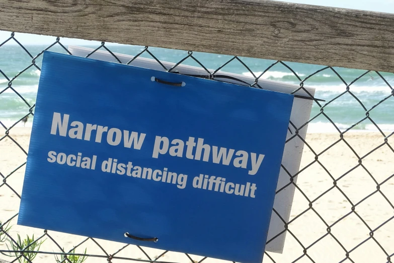 the blue sign is sitting in front of a fence on the beach