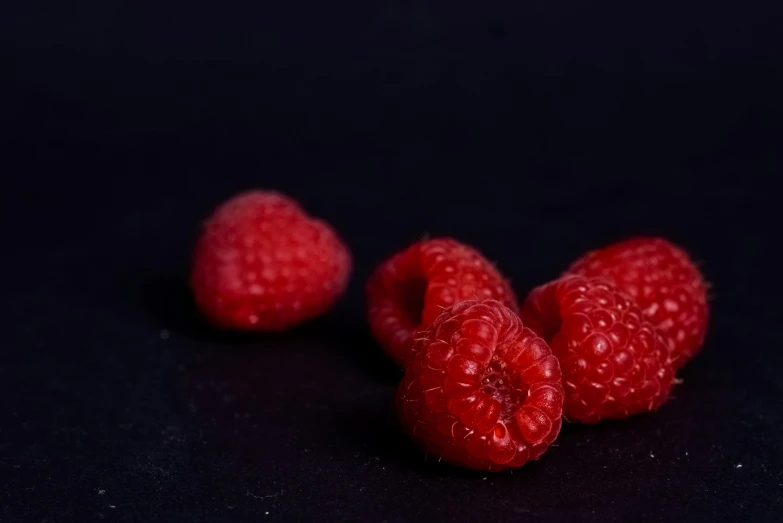 three raspberries sit in front of a black background
