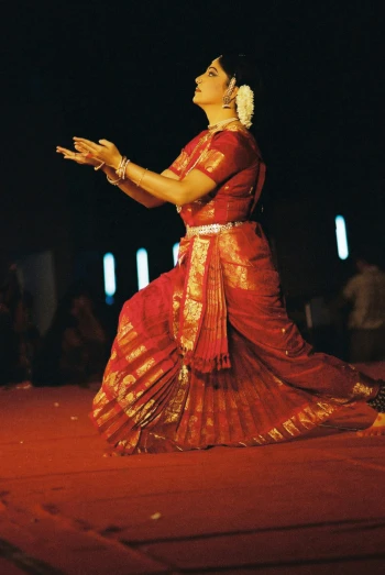 a woman in a red saree with her hands crossed and clapping on the floor
