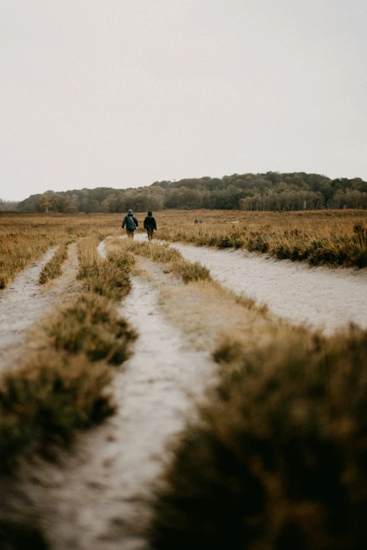 two people are walking down a path in an open field