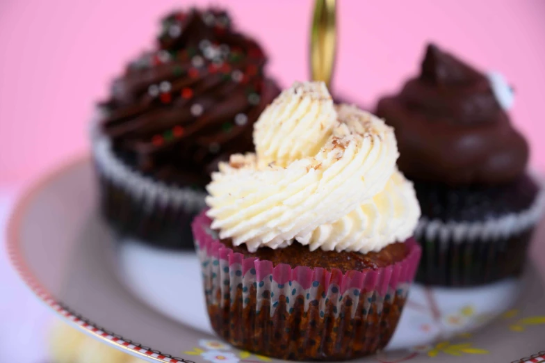 three cupcakes with icing on a white and pink plate