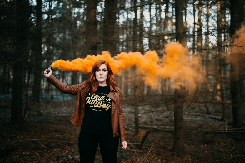 a woman wearing a brown jacket and black pants standing in front of yellow smoke