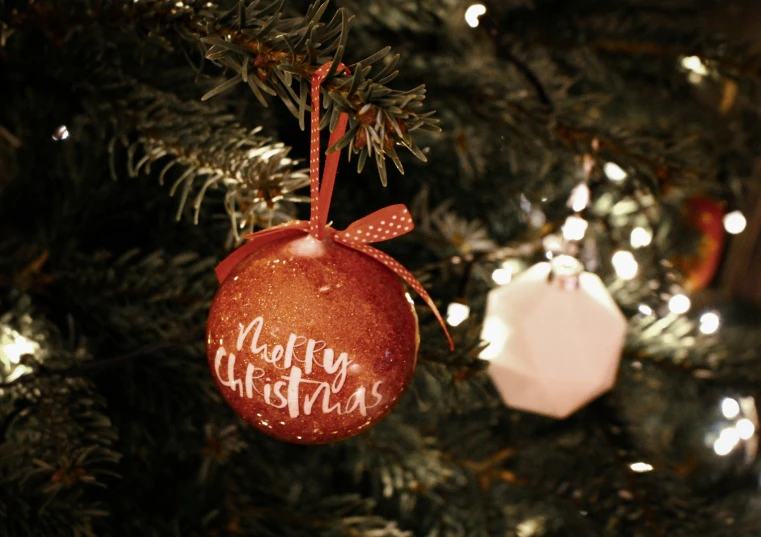 a christmas ornament with a merry christmas message hanging from a tree