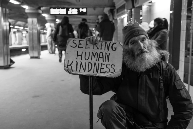 a homeless man holding a sign that says seeking human kindness