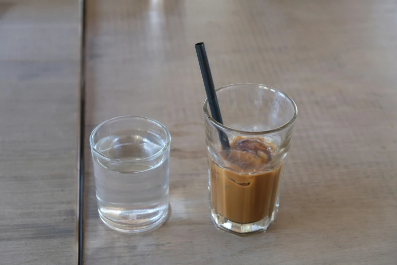 glass and tumbler on wooden table containing beverage