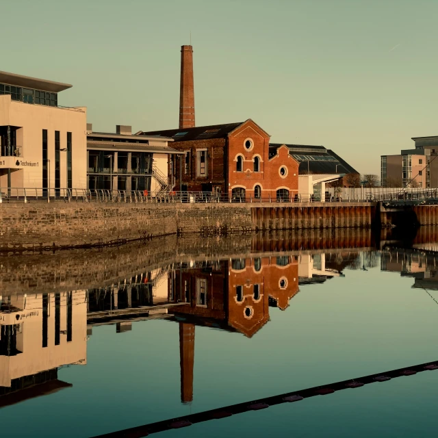 a small factory sits in a river with reflections on the water