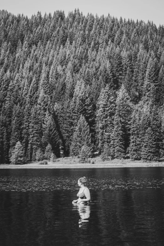 black and white pograph of man swimming in lake surrounded by trees