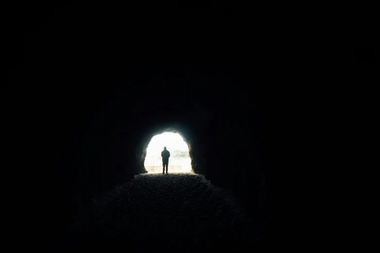 person in silhouette at the end of a dark tunnel