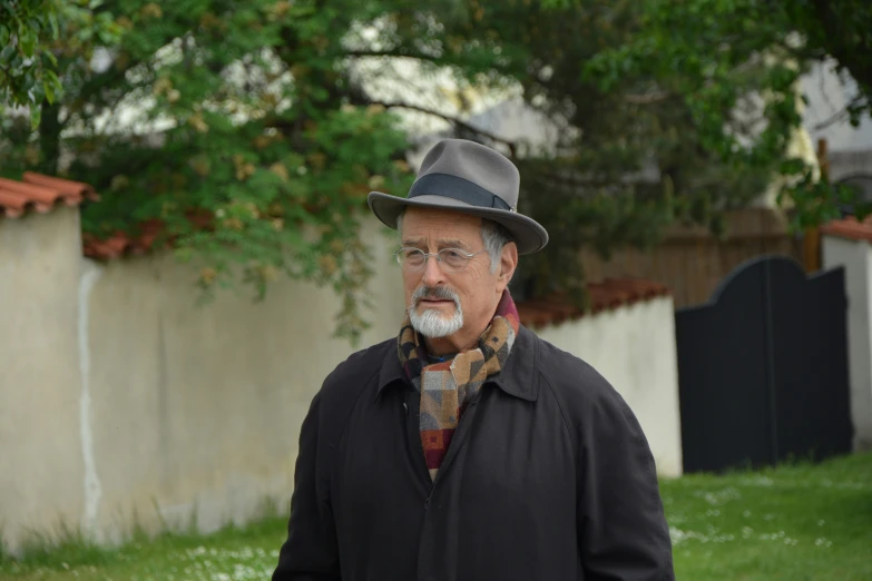 an old man wearing a hat and coat walks by a fence