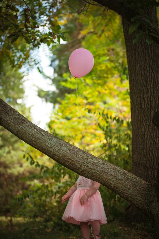 little girl in pink dress holding a pink balloon with white strings