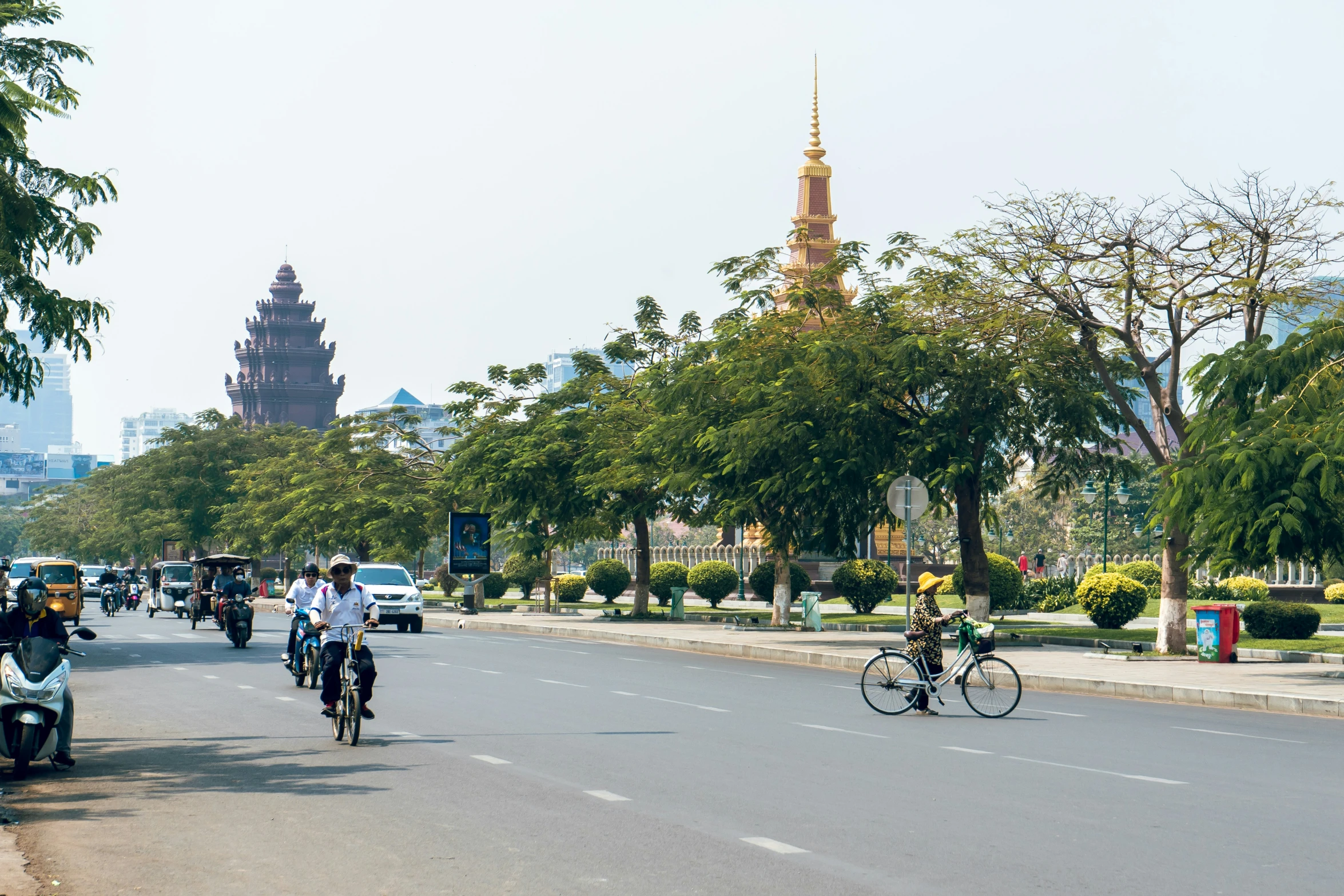 several people on bikes, on a street next to a tower