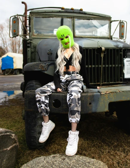 a person wearing a green mask sitting on the front tire of a truck