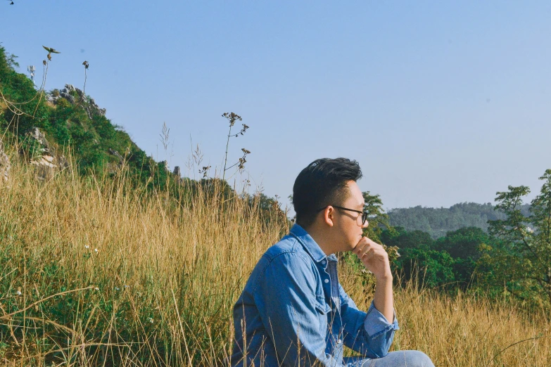 an asian man sitting on the edge of a mountain