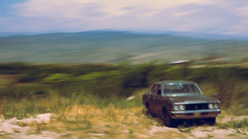 an old car in the grass near a hill