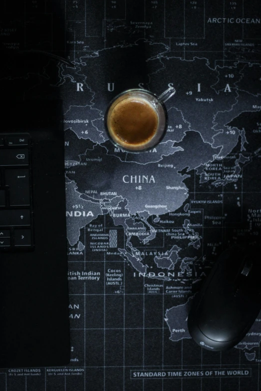 a mouse, mouse pad, and a glass with liquid are in front of the world map