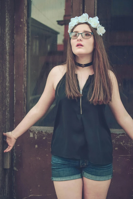 a girl with glasses and a flower in her hair posing in front of a door