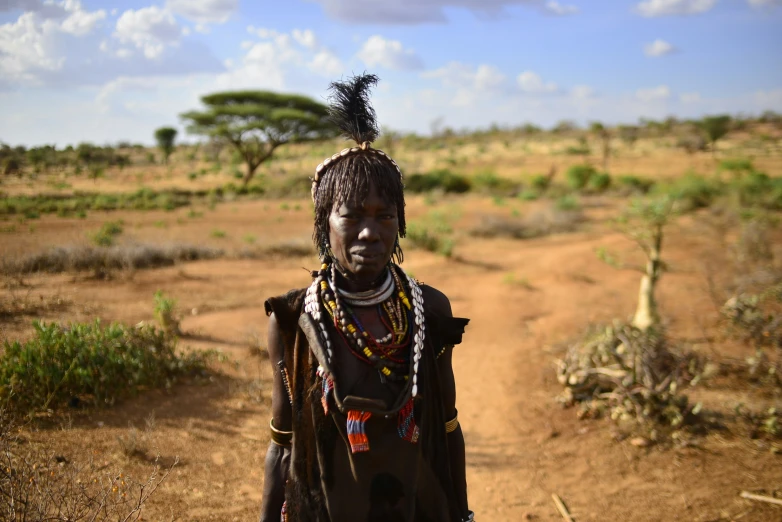 a woman in native garb stands on a dirt road