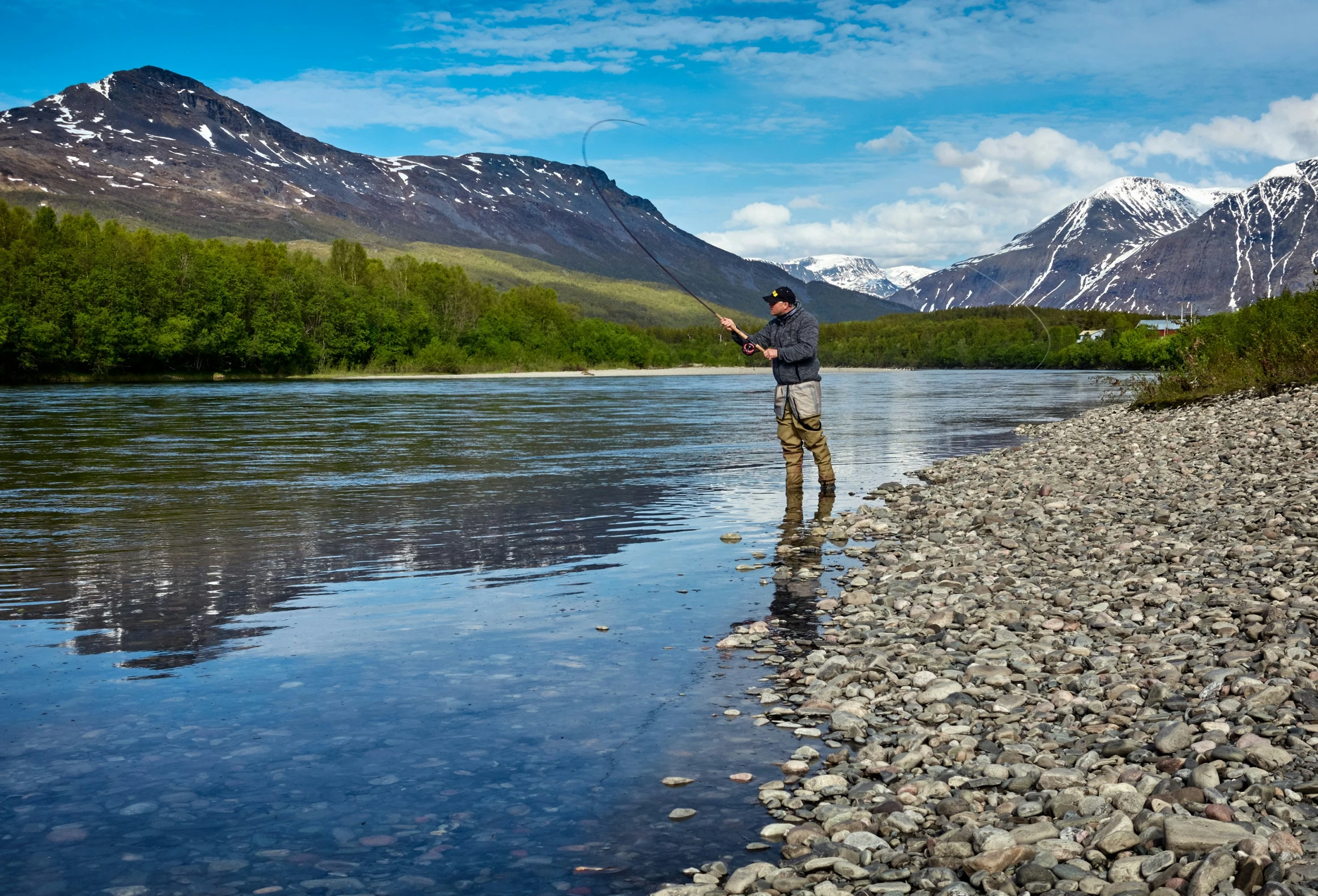 a man standing on the edge of a body of water holding a fishing pole