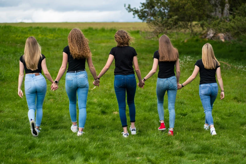 a bunch of women in tight jeans are standing on some grass