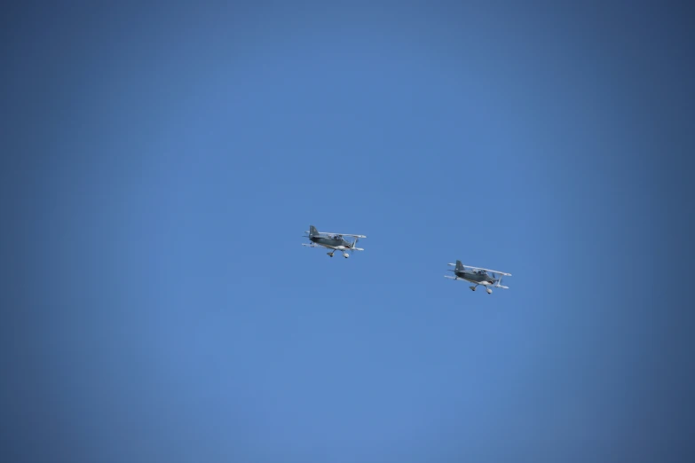 two airplanes flying across a blue sky with one flying sideways