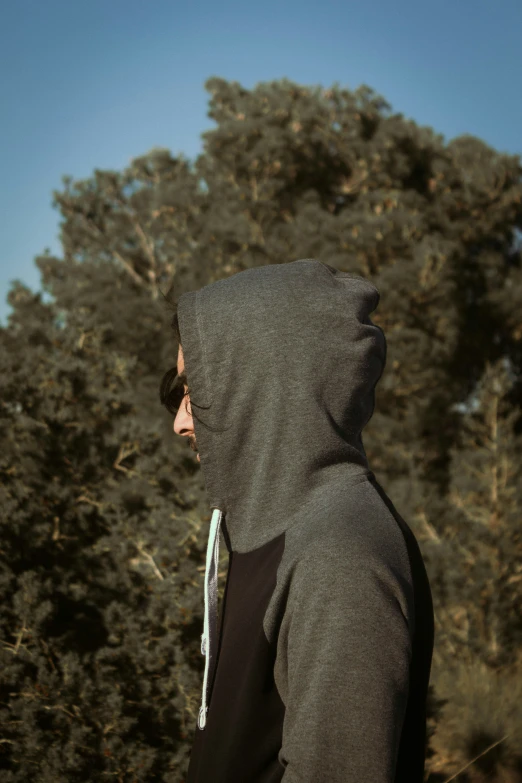 man in hooded hoodie stares over treetops