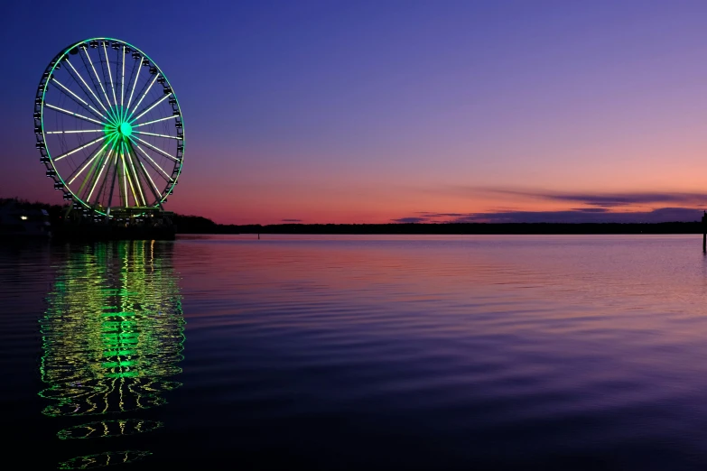 a ferris wheel lit up during sunset near a river