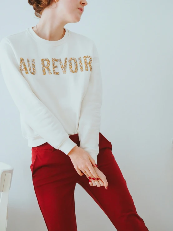 a woman is posing in red pants and a white sweatshirt