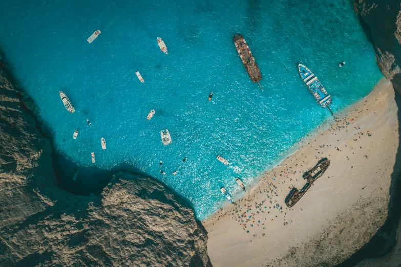 an aerial view of a blue water beach with several boats in the distance