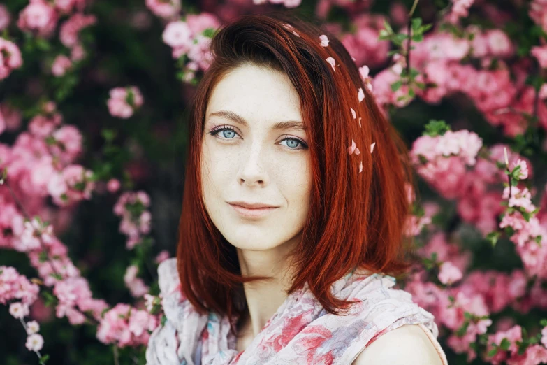 a woman with red hair standing in front of flowers